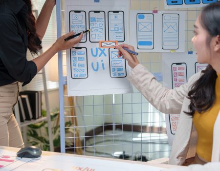 Two female web designers engaging in a discussion about user interface and user experience while reviewing mobile application wireframes in a modern office setting